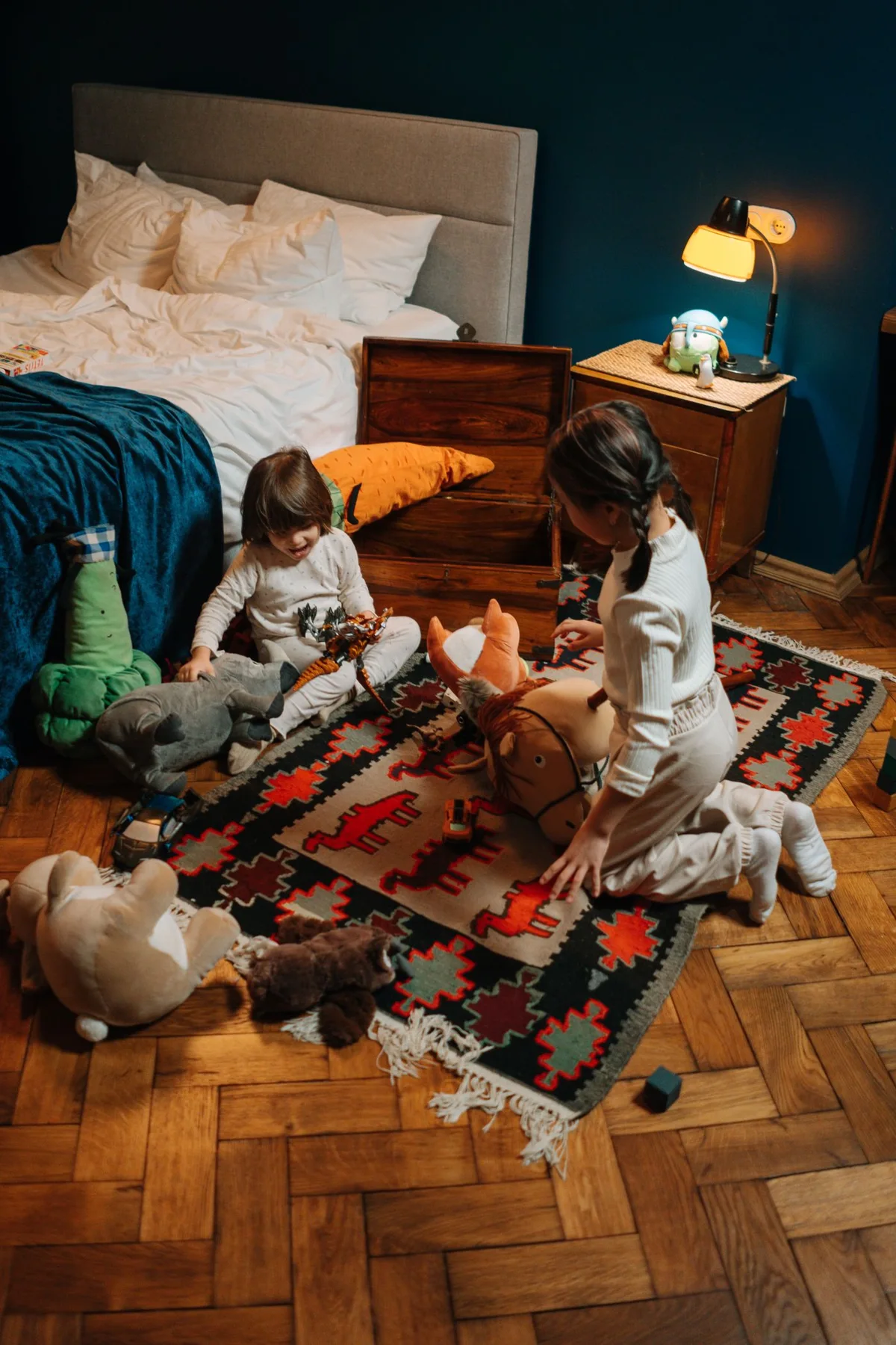 Two children in pajamas playing with soft toys on a bedroom floor