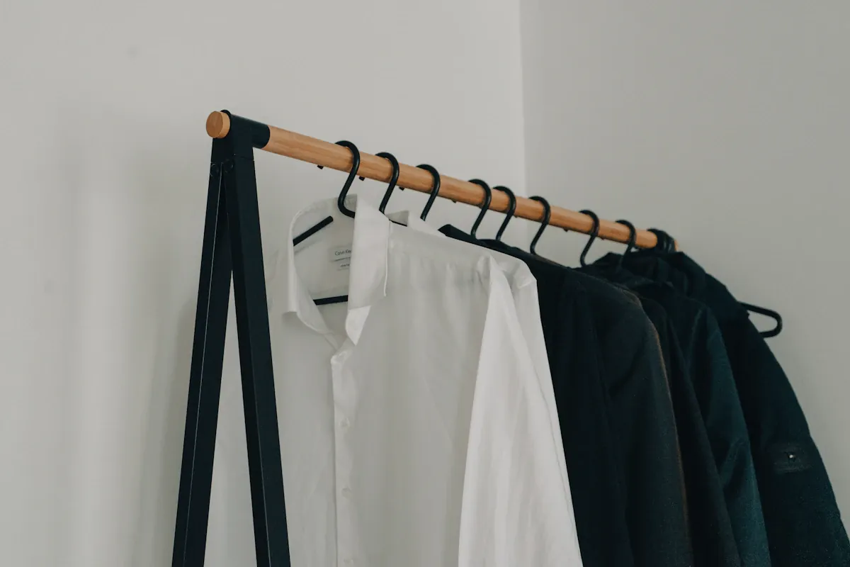 White and dark garments hanging together on black hangers and a wooden rail