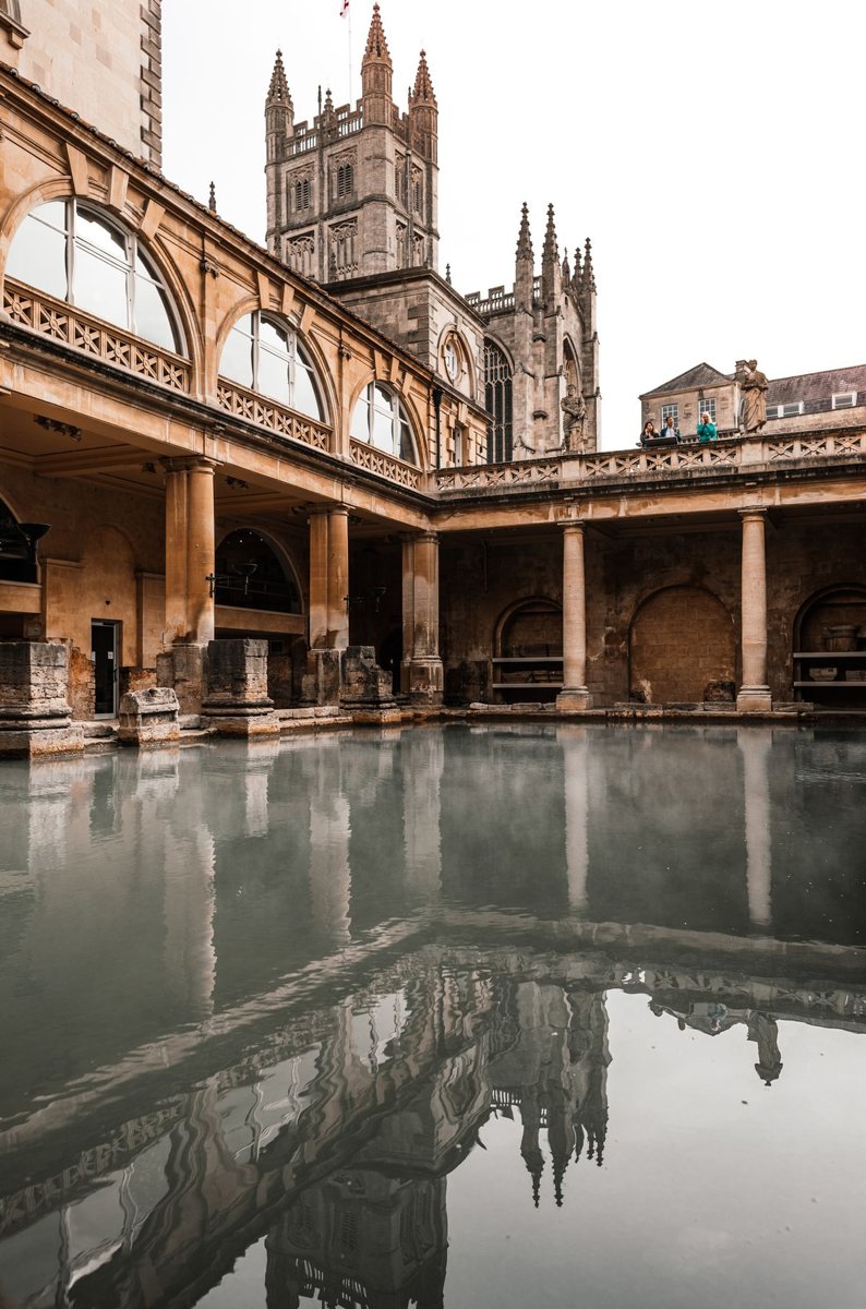 Historic stone buildings reflected in the Roman Baths in Bath, England