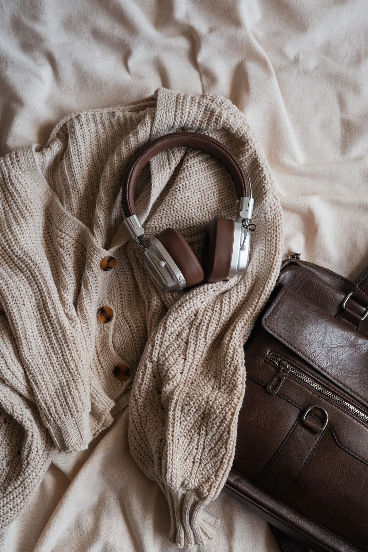 Headphones beside a knitted garment and a brown bag