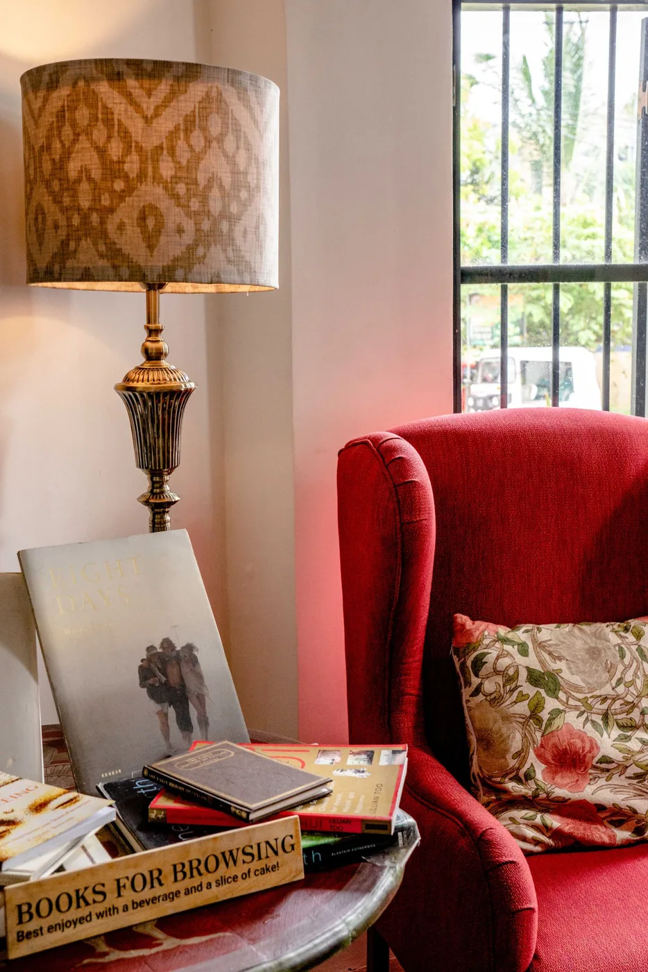 Red upholstered chair beside a lamp, window and a small table with books