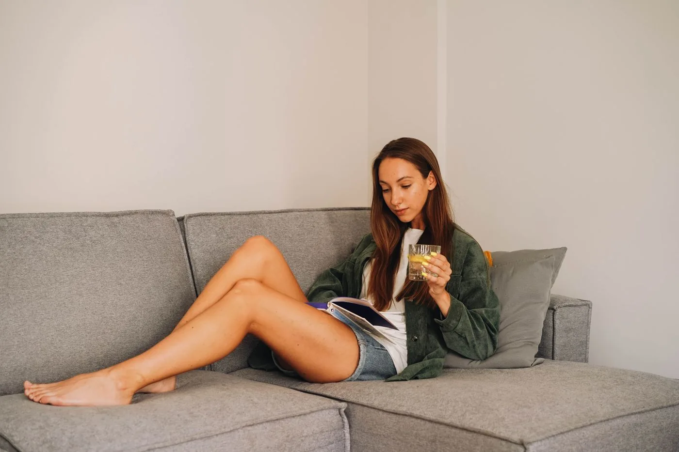 Woman reading a book while seated on a grey sofa
