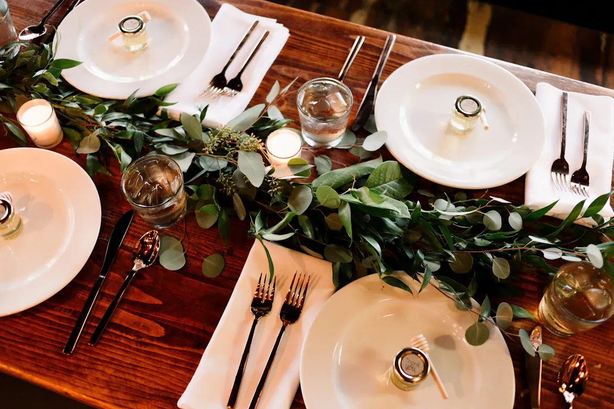 White plates, folded napkins and cutlery arranged beside greenery on a table