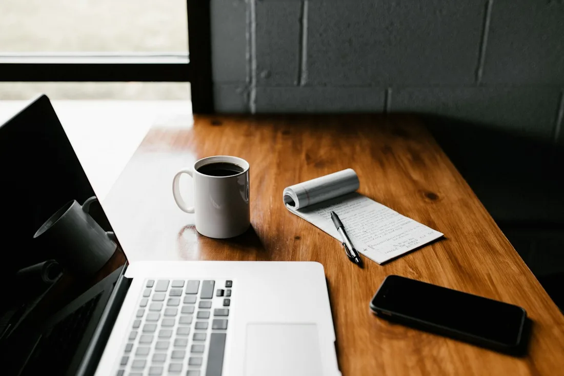 Laptop, notebook, mug and phone arranged on a wooden table