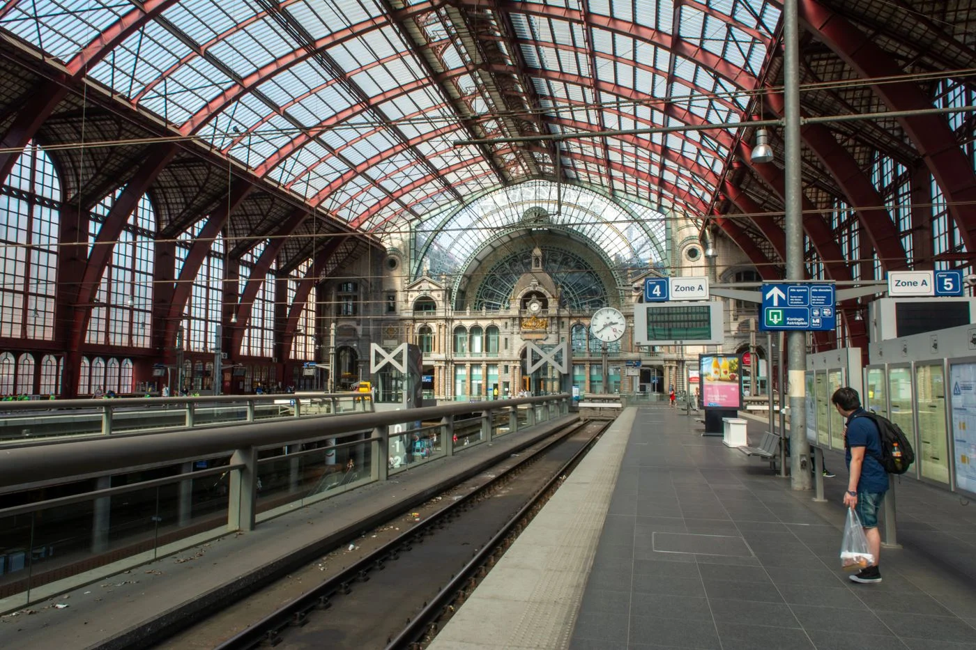 A passenger on a platform beneath the roof of Antwerp Central Station.