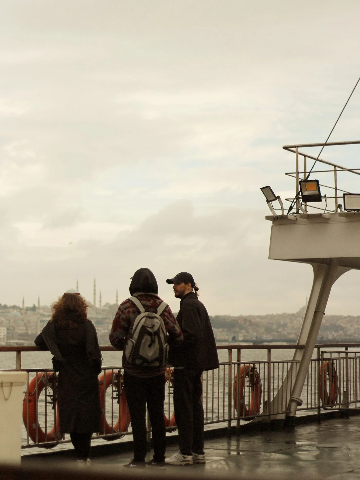Three people standing on a ferry deck looking across the water.