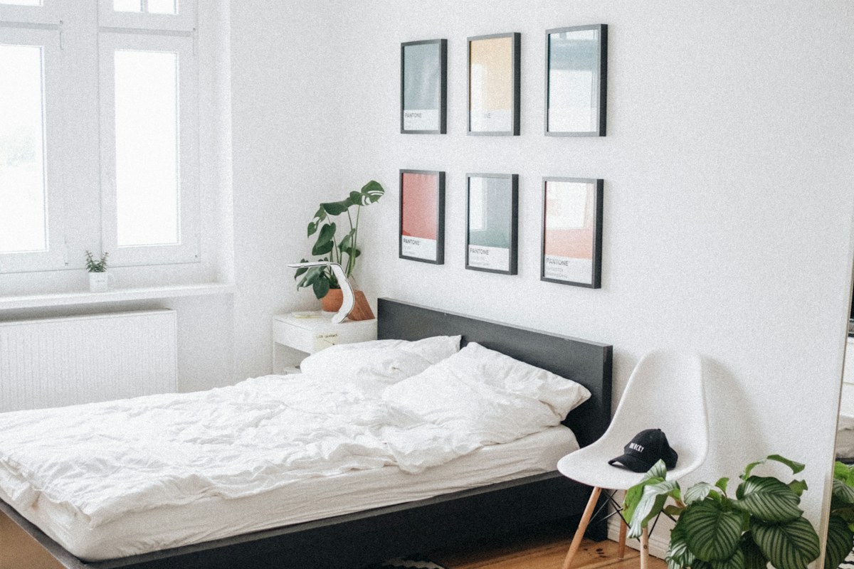 A bed with pale bedding in a bright bedroom.