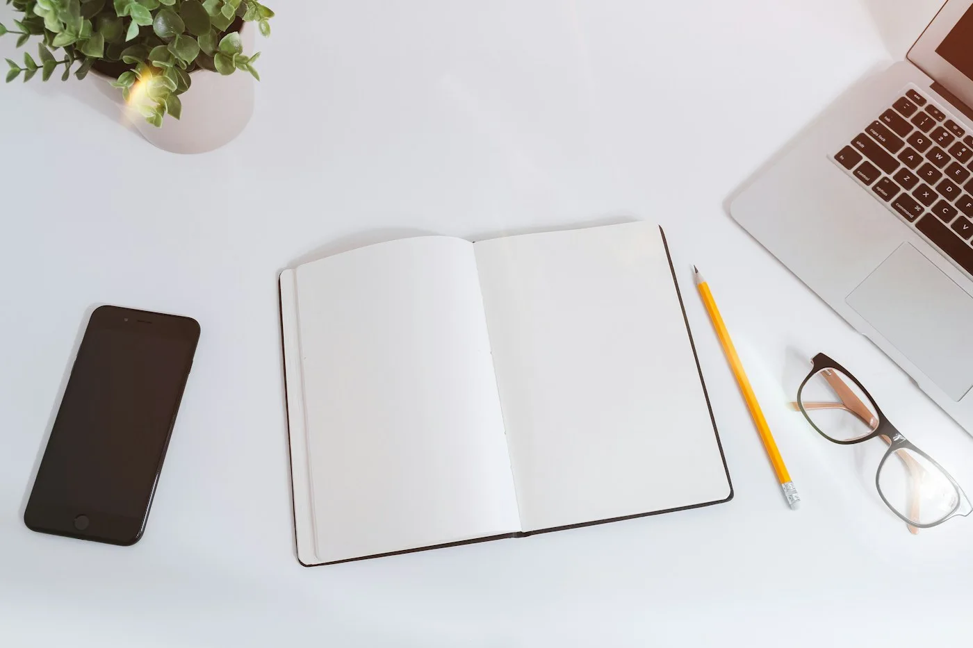 An open notebook, pens, glasses, and devices on a desk.