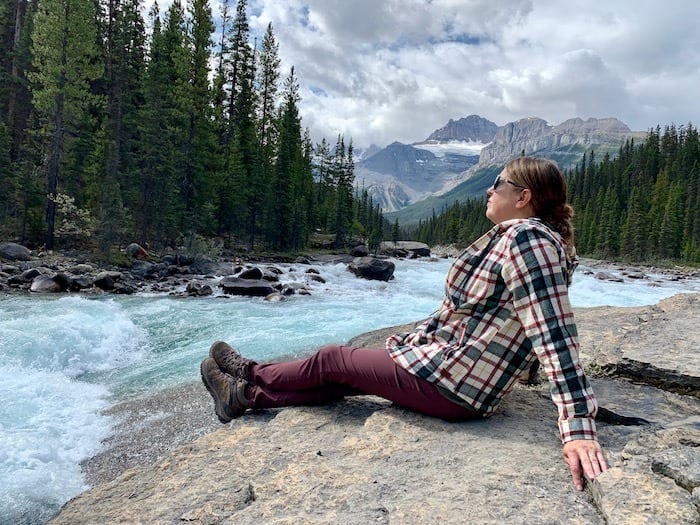 woman in plaid shirt sitting on rocks at Mistaya Canyon