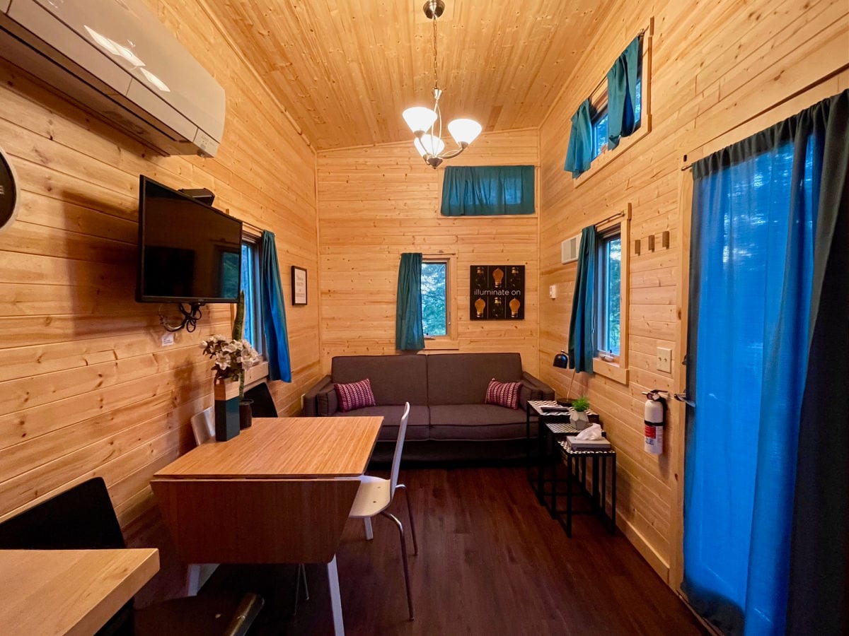 Emerson tiny house living room with sofa and kitchen table and chairs with wood walls and blue curtains