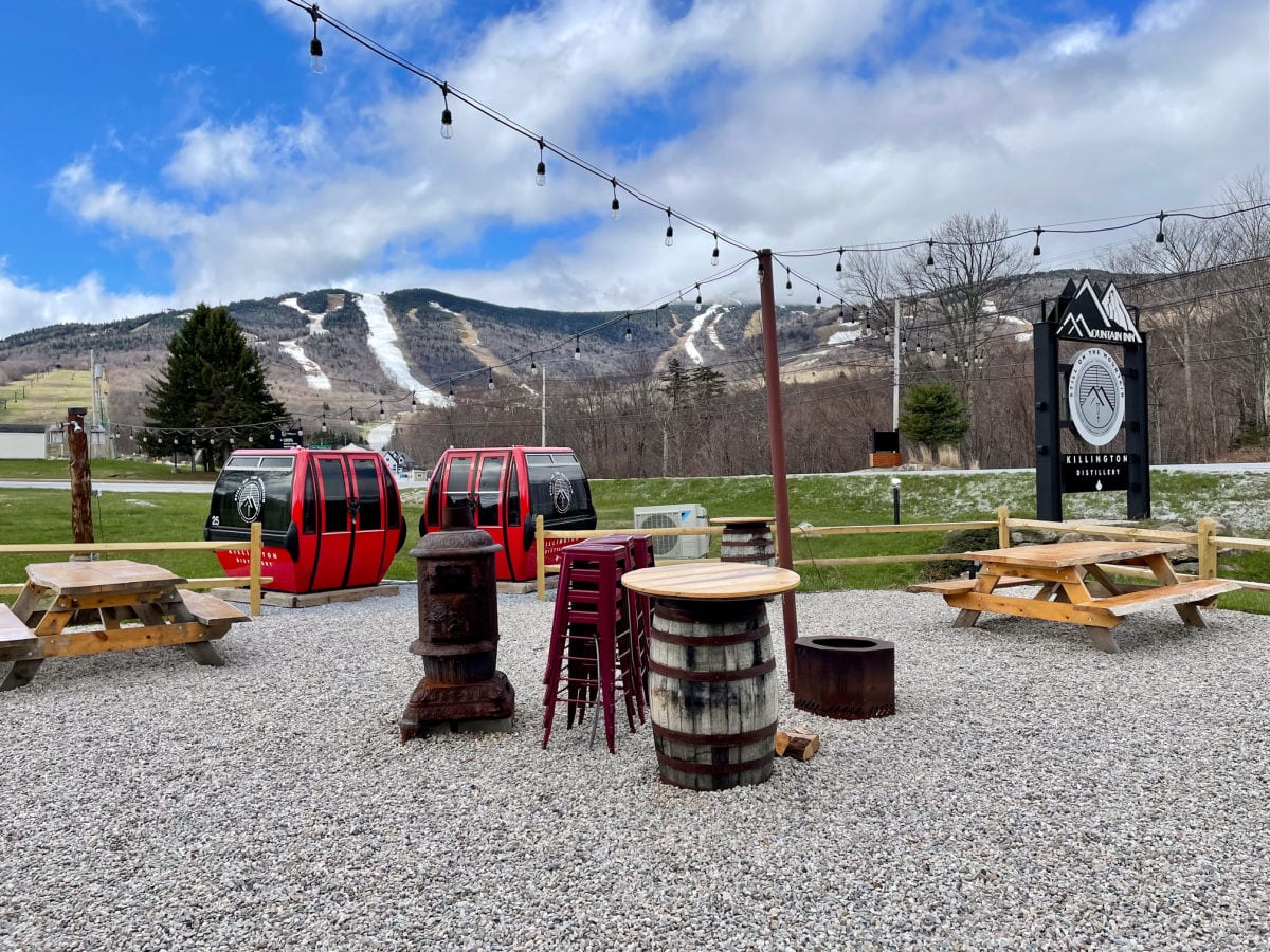 Mountain Inn sign and outdoor patio with two red gondolas, picnic tables and a view of the ski runs on Killington