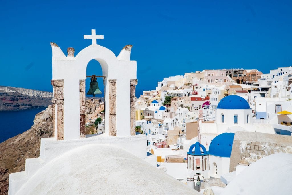 Oia town on cliff with church bell and blue dome in the foreground