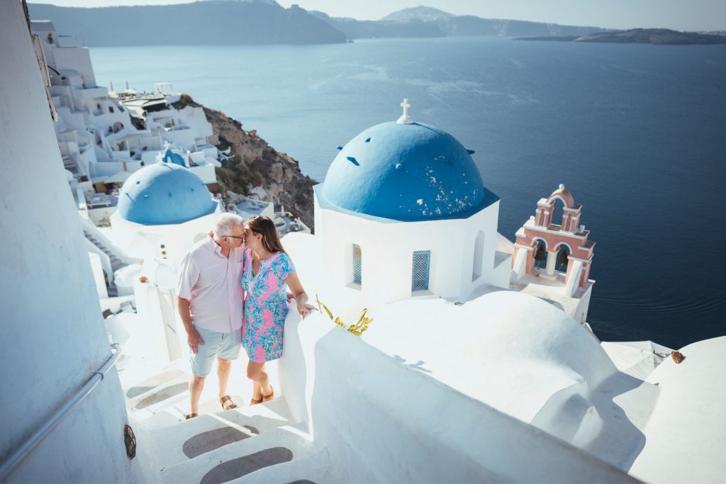 Couple kissing in front of two blue domed churches in Oia Santorini