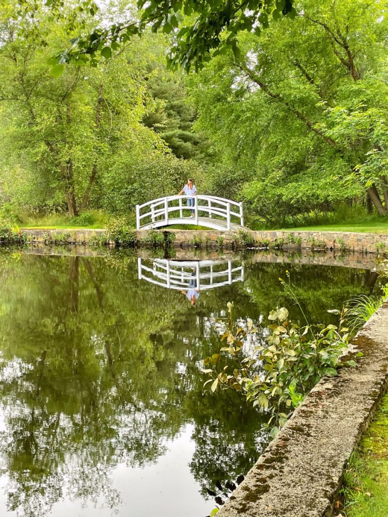 woman on white bridge overlooking pond with reflection in the water