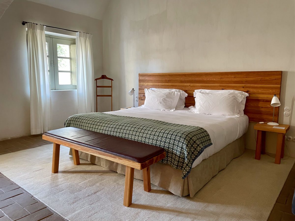 Queen bed with white sheets, green checked blanket, and wooden headboard
