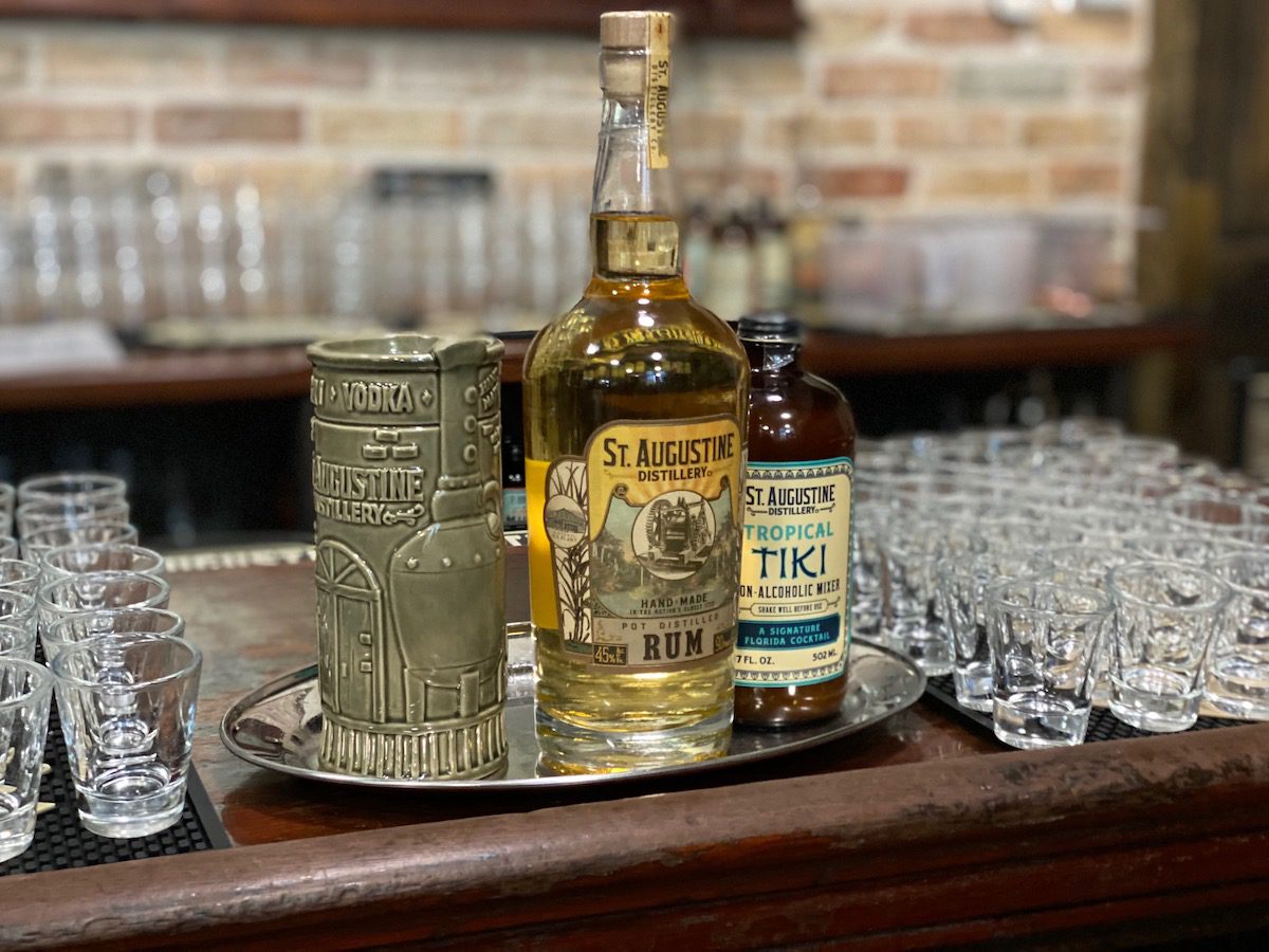 St Augustine rum bottle with small shot glasses and a tropical tiki mixer bottle