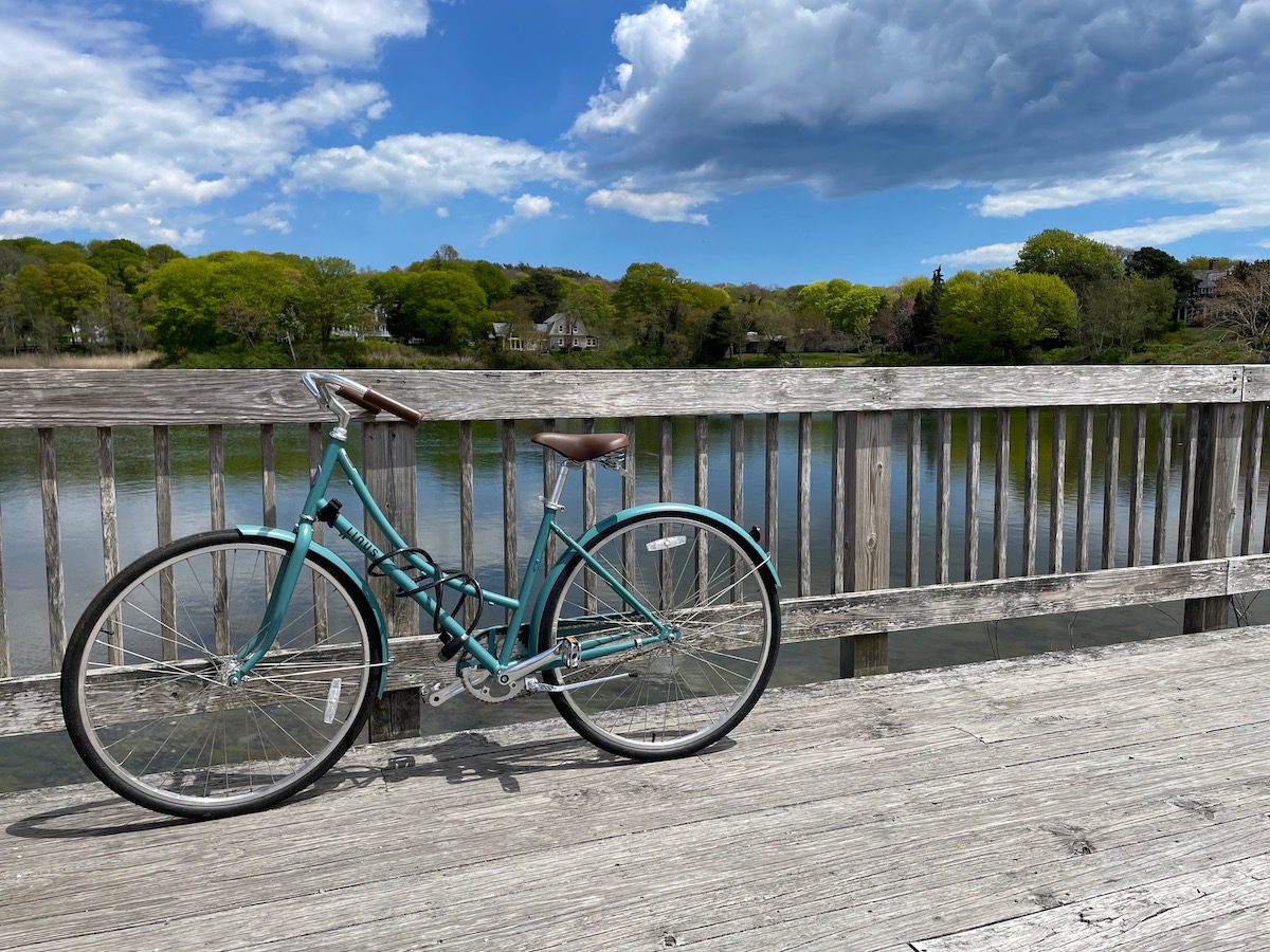Blue bike with brown seat leaning against wooden rail in front of the water