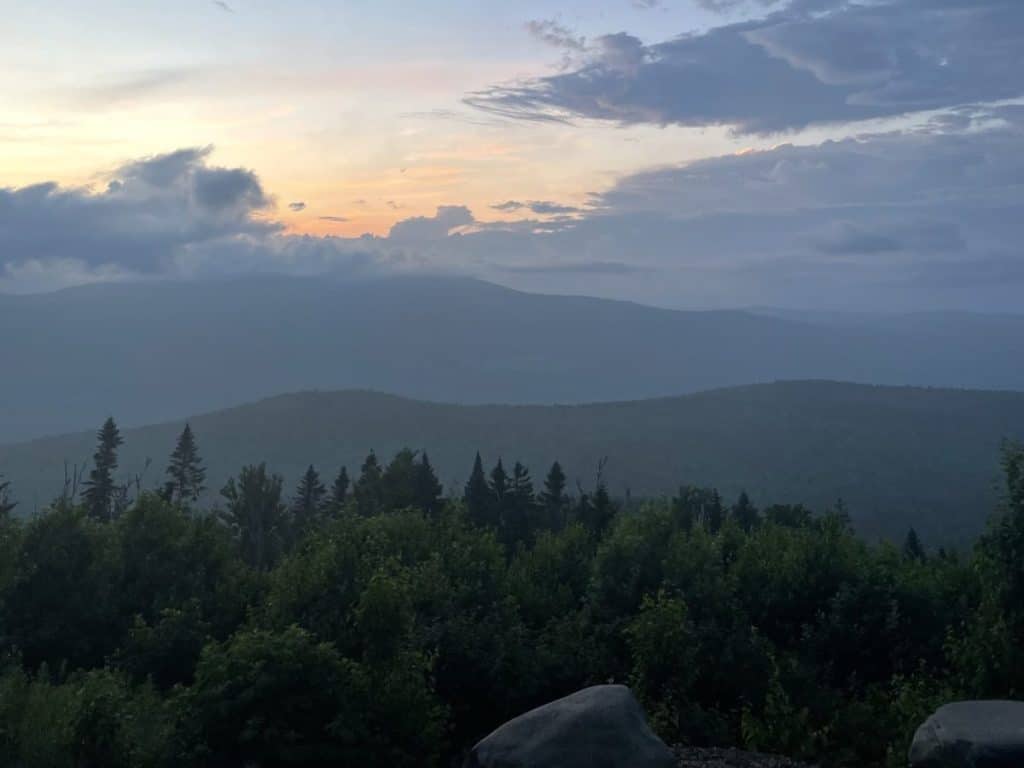 view of a mountain range in the distance with pine trees and large rocks in the foreground