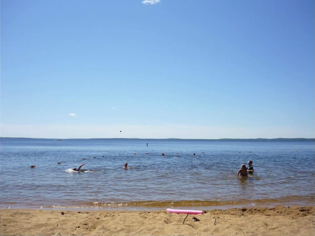 Sebago Lake beach front kids swimming in the water close to shore with distant mountains in the horizon