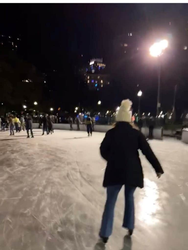 Women skating on rink with city buildings in the background.