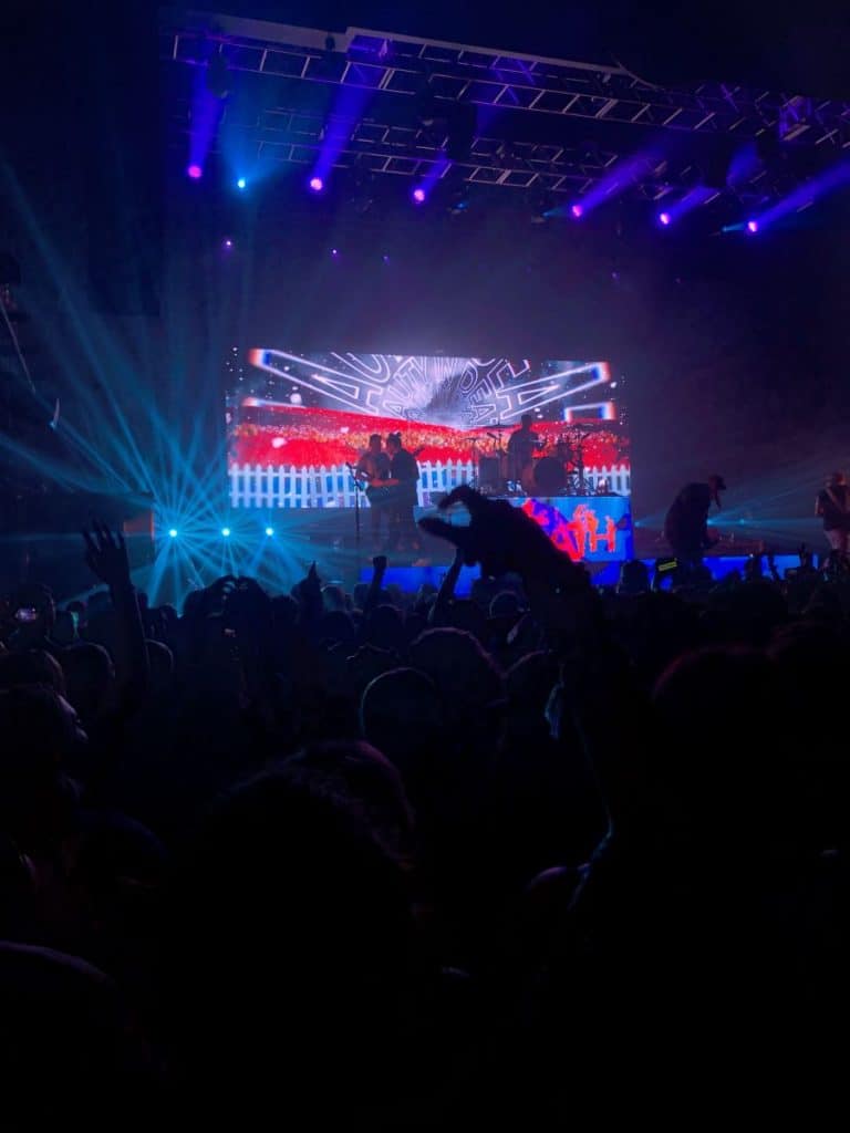 Dark concert arena with band playing instruments on stage.