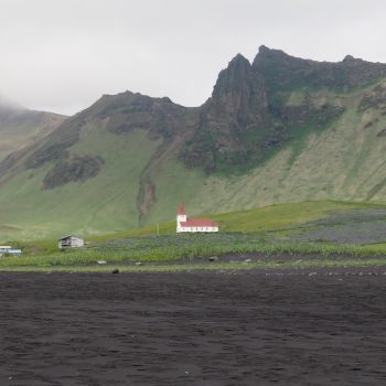 White church with red roof on a background against the green cliffs in Vik Iceland