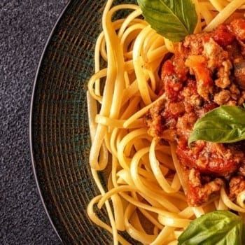 Bowl of pasta with tomato sauce and basil on dark grey background