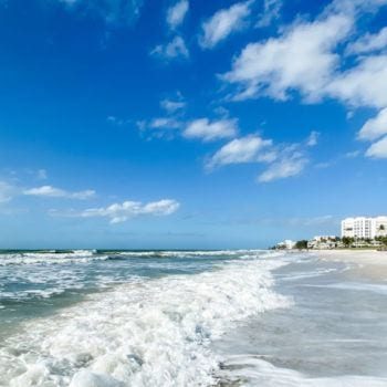 Lowdermilk beach waves crashing on the sand with hotels in the background and bright blue sky