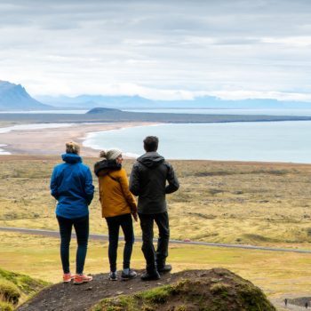 3 people standing on hill looking out at Icelandic landscape